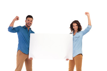 excited young casual couple holding blank board and celebrate success