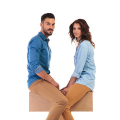 young casual couple sitting together on wooden box