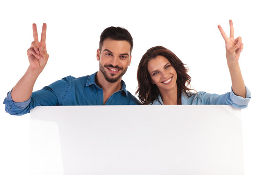 happy young casual couple makes  vicory  sign over  blank board