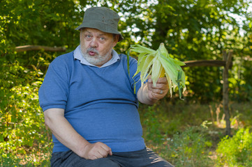 Positive portrait of senior farmer giving ripe ear of maize