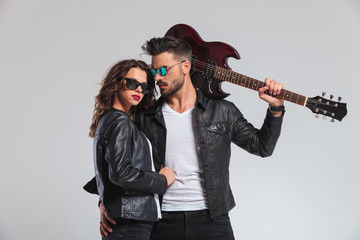 cool punk man holding guitar on shoulder and embracing woman