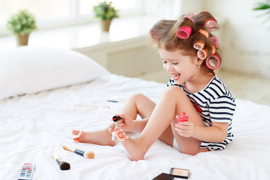 Happy funny child girl with hair curlers does a pedicure, paints nails and laughs