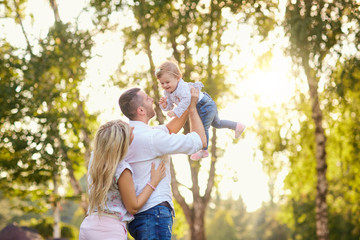 Mother father play with the baby in the park in the autumn summer. Parents raised the baby over his head.