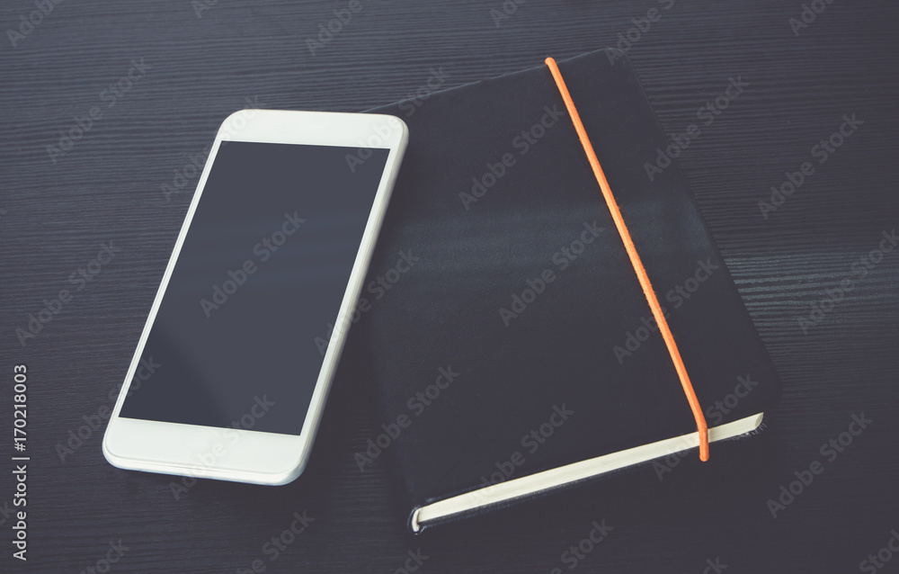 Poster Blank screen of mobile phone lay on black notebook near window on black wooden modern desk at afternoon sunlight, Mock up for display of design or content,Clipping path smart phone screen