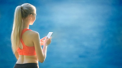 young blonde woman stands on a blue sea background with a mobile phone. A sporty woman uses a phone near the sea