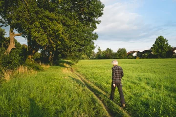 Cercles muraux Campagne Old man walking in a green field during the sunset in the countryside.