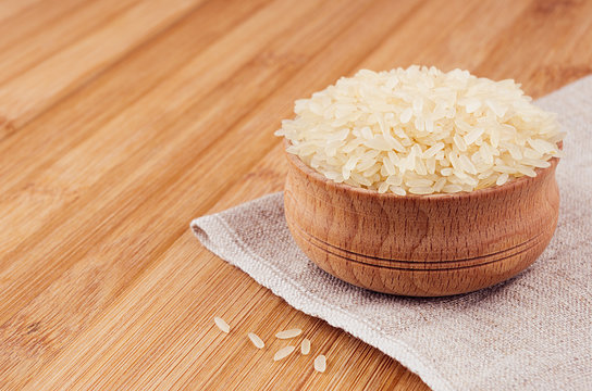 White rice basmati in wooden bowl on brown bamboo board, closeup. Rustic style, healthy dietary cereals  background.