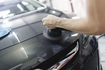 Car detailing - Hands with orbital polisher in auto repair shop. Selective focus.