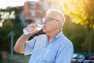 Outdoor portrait of senior man who is drinking water.