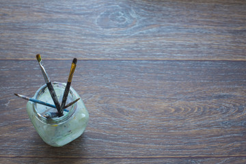 Artist brushes in a glass jar, on dark wooden background.