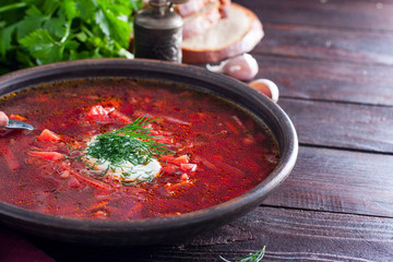 National traditional Ukrainian soup made from beets and vegetables - borscht with sour cream and fresh herbs in a clay bowl, horizontal, copy space