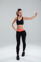 Fototapeta na wymiar Full length picture of fitness woman posing and making selfie
