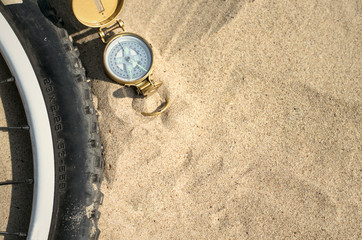 Fototapeta na wymiar Compass and bicycle wheel on the sand ground. Travel concept.