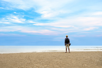 Young traveler man with backpack standing at seaside and looking to the ocean