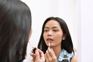 Beautiful asian girl applying lipstick while looking on the mirror