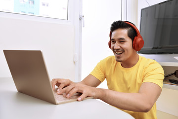 Happy asian man sitting with laptop and headphones