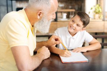 Grandfather holding grandsons pencil while helping him with homework