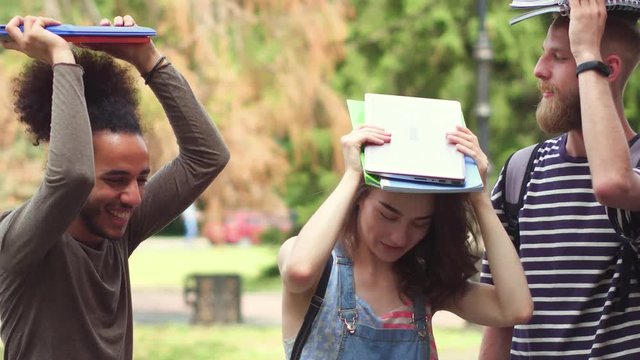 Students having fun, holding notebooks on their heads. Leisure time of college friends.