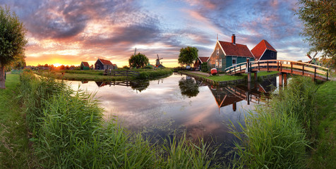 Panorama landscape windmills on water canal in village. Colorful spring sunset in Netherlands, Europe