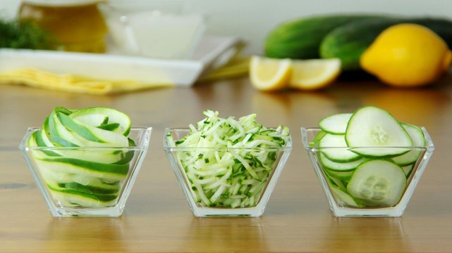 Sliced and spiralized cucumber prepared for salad. Other ingredients on background. Close up view.