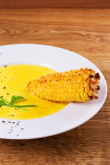 Cream corn soup in bowl and corn on cob on wooden background