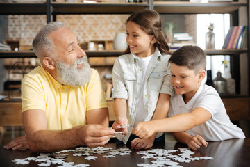 Siblings and their grandfather having fun while doing puzzle