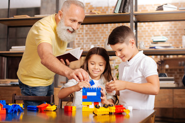 Grandfather helping grandchildren build a tower with construction set