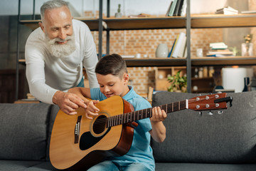 Happy grandfather giving grandson tips on playing guitar