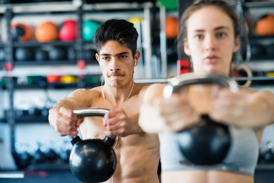 Young fit couple in gym exercising with kettlebell.