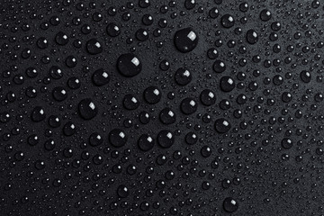 Water drops on black grainy surface, dark background