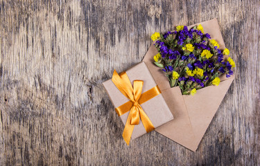 Bright wild flowers in a paper envelope and a gift with a golden ribbon on a worn wooden background. Backgrounds and textures.