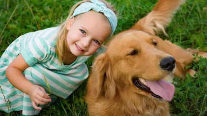 Adorable smiling little blond girl playing with her cute pet dog golden retriever