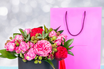 Beautiful bouquet of pink and red roses and red ribbon in a circular black box near pink gift bag