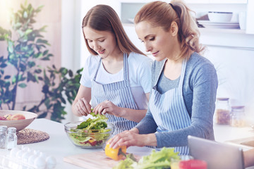 Cheerful family members making delicious vegetable salad together at home
