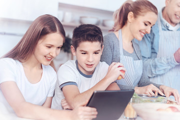 Charming kids playing on digital tablet while parents cooking