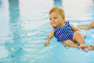 Fototapeta na wymiar Cute little baby child learning to swim in an indoor pool
