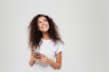 Smiling pensive woman holding smartphone in hands and looking up