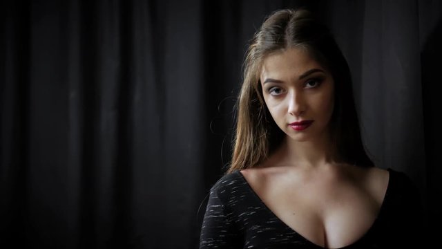 Sensual woman with makeup and red lips. A young girl is exhaling smoke on a black studio background.
