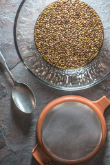 Glass bowl with cannabis seeds, a sieve and a spoon on a stone