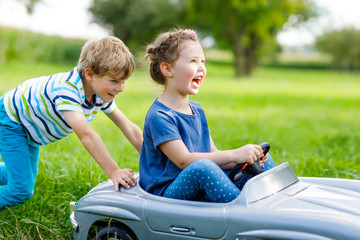 Two happy children boy and girl playing with big old toy car in summer garden, outdoors