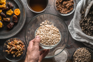 Hand with a bowl of oats and ingredients for the granola