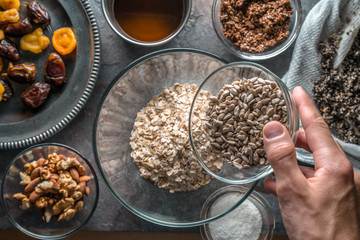 Hand with a bowl of seeds, ingredients for the granola and mixing bowl