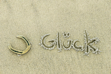 ein Hufeisen und das Wort Glück im Sand