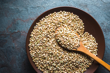 Wooden spoon in a plate with raw green buckwheat