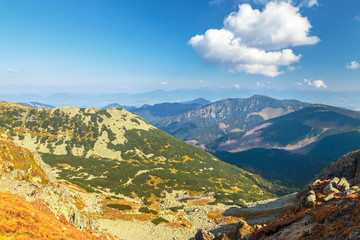 View from the ridge of the Low Tatras National Park in Slovakia to the mountain landscape with hills and valleys, during a sunny day with clouds in the blue sky.