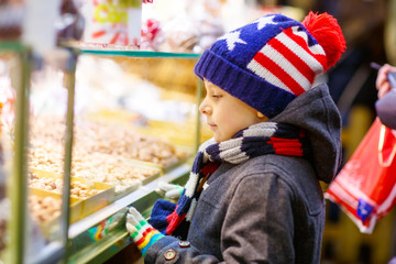 Little kid boy with gingerbread and sweets stand on Christmas market