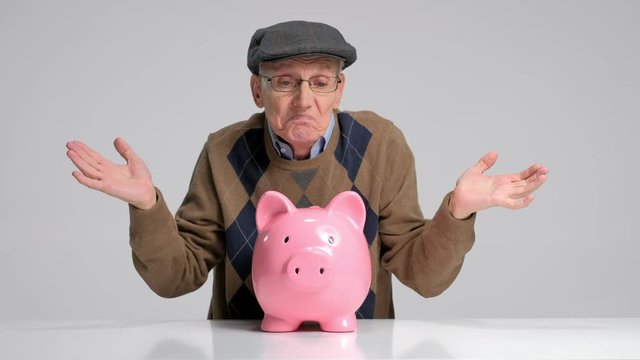 Depressed senior with a piggybank gesturing with his hands