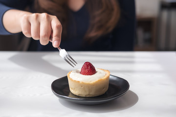 Closeup image of a woman using fork to cutting strawberry cheese tart on white vintage wooden table in cafe