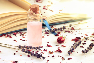 Glass corked bottle of pink perfumed water, book, dried lavender twigs, soft light shining, toned. 