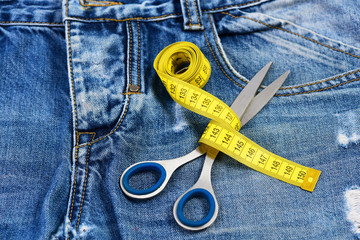 Tailors tools on denim: measure tape wound around metal scissors
